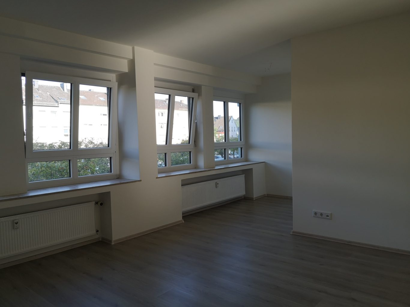 Immobilienmakler Münster Helle, leere Wohnung mit großen Fenstern und Holzfußboden.