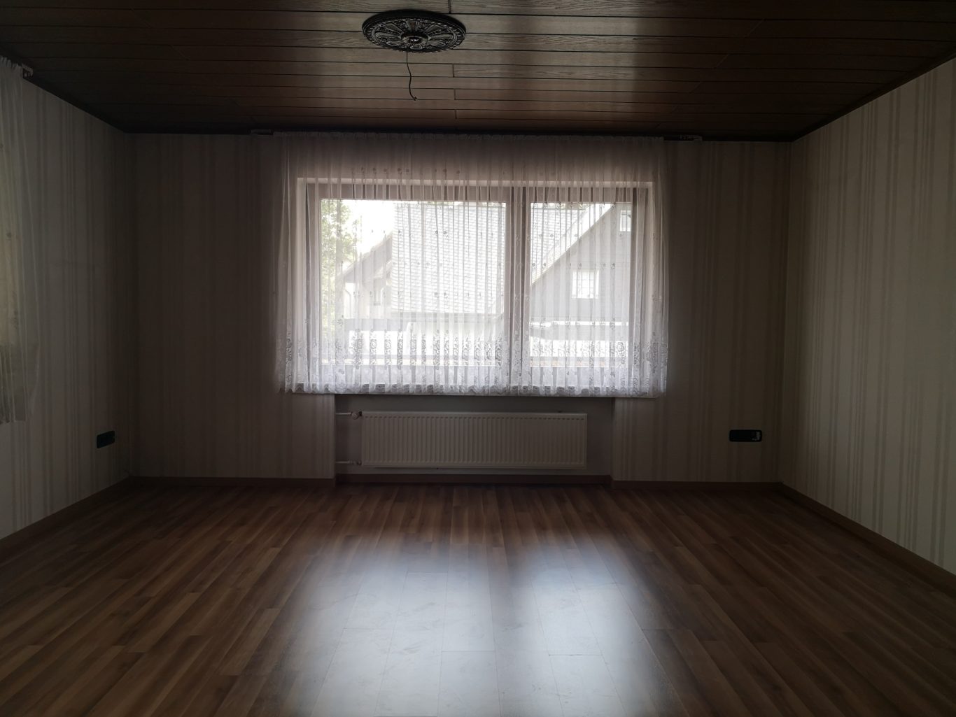 Immobilienmakler Münster Heller, leerer Raum mit Holzfußboden und Fenster mit Vorhang.