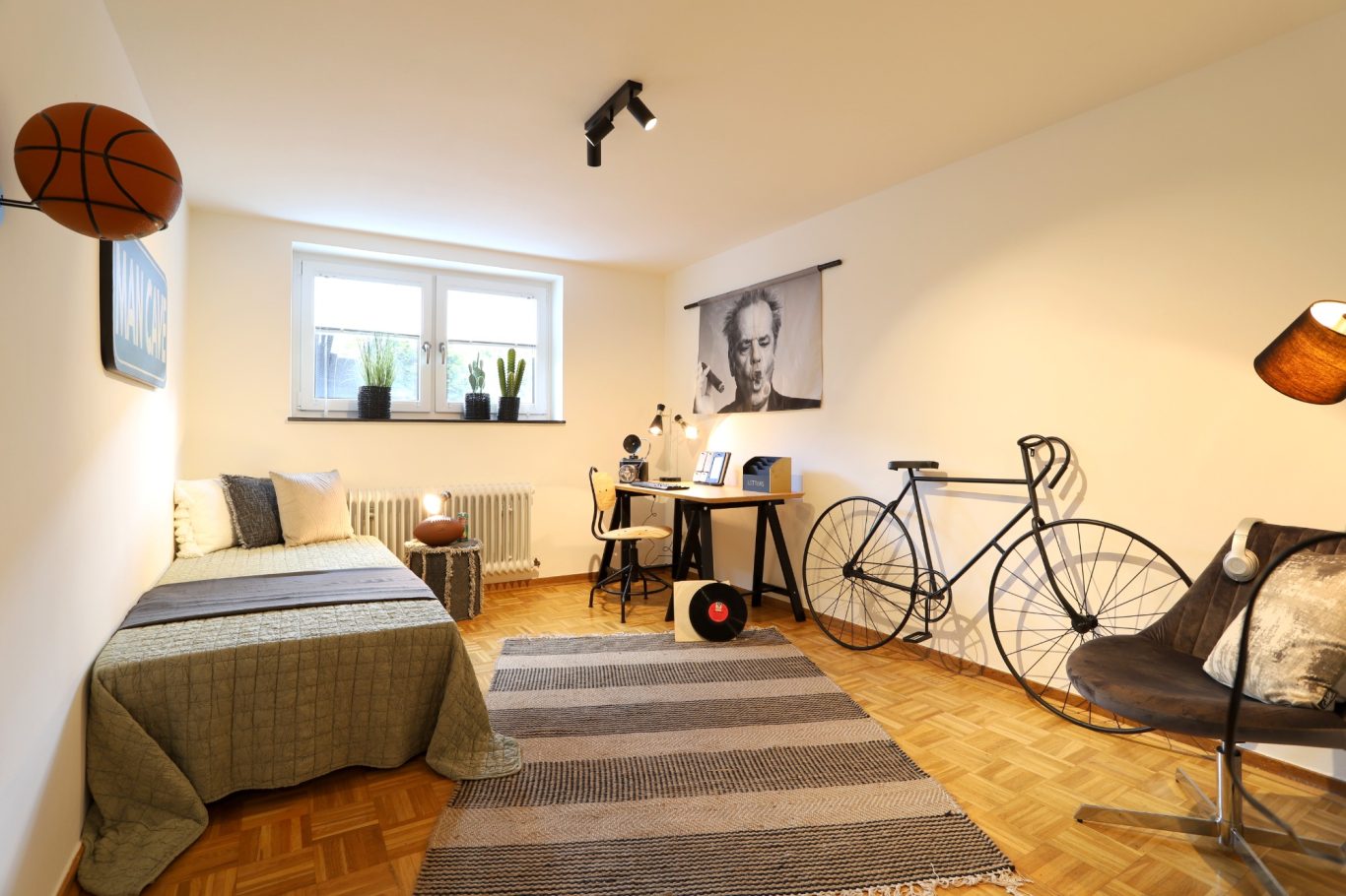 Wohnung Kaufen Ein modernes Schlafzimmer mit Bett, Schreibtisch, Fahrrad und Basketball-Dekoration.