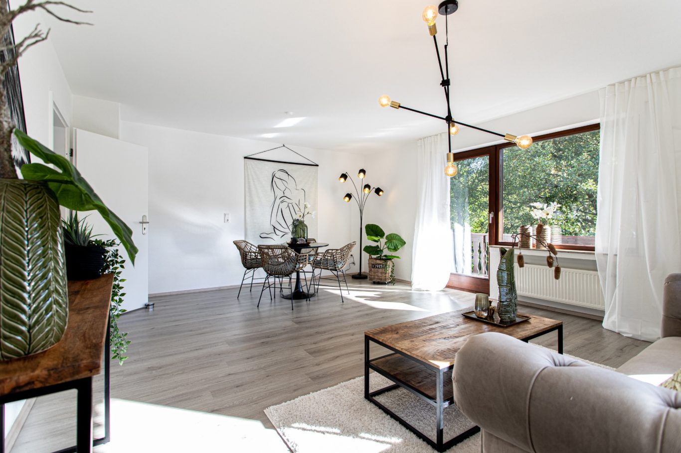 Immobilienmakler Münster Helles Wohnzimmer mit modernen Möbeln, Pflanzen und großem Fenster.