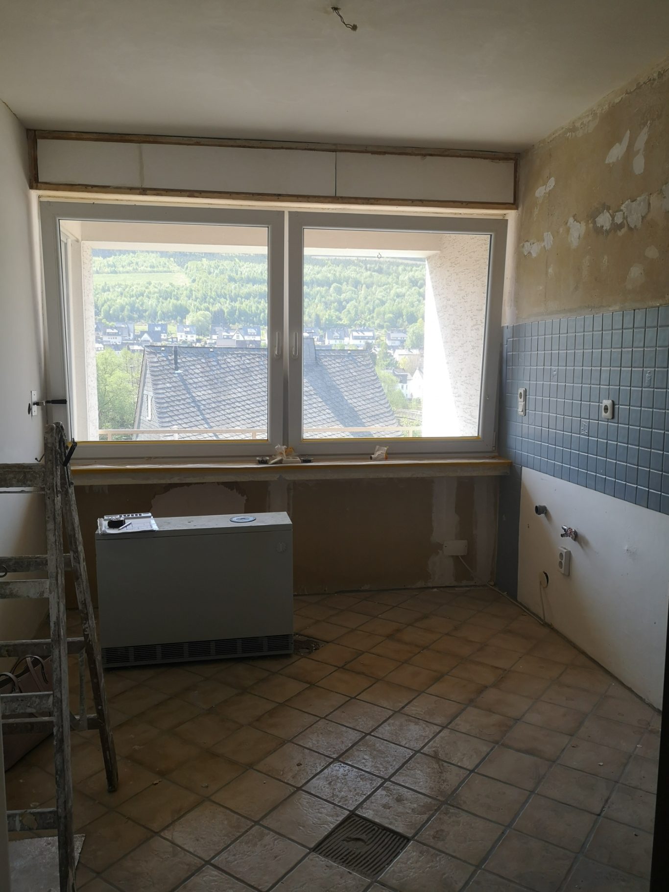 Immobilienmakler Münster Leere Küche mit großen Fenstern, Fliesenboden und unvollendeten Wänden.