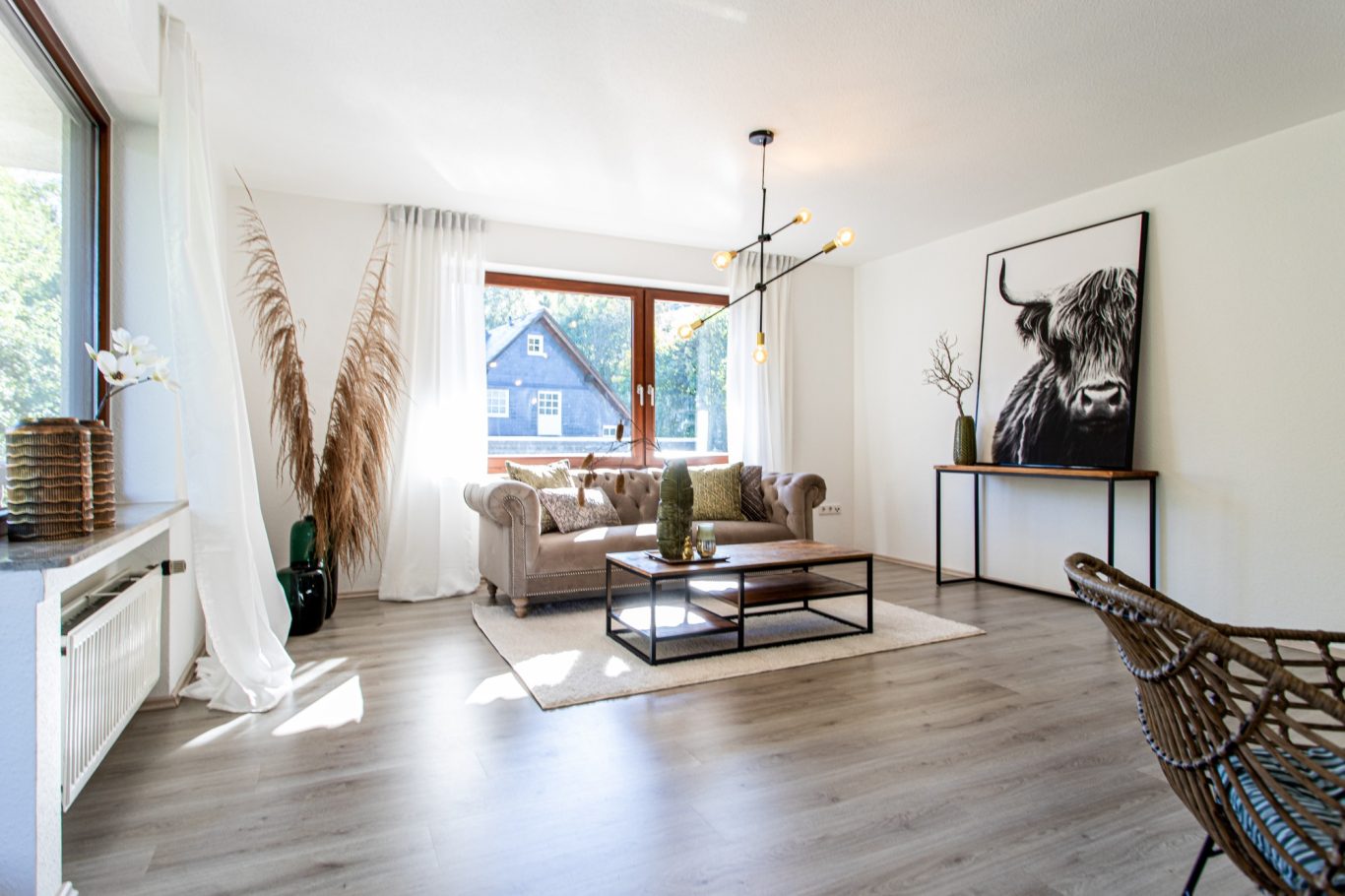 Immobilienmakler Münster Heller Wohnraum mit modernem Mobiliar, Pflanzen und einem großen Kunstwerk an der Wand.