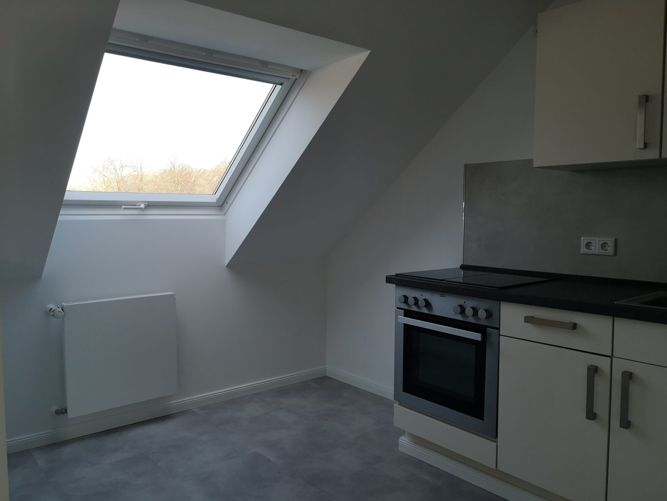 Immobilienmakler Münster Küche mit Dachfenster, Herd, grifflosen weißen Schränken und grauem Bodenbelag.