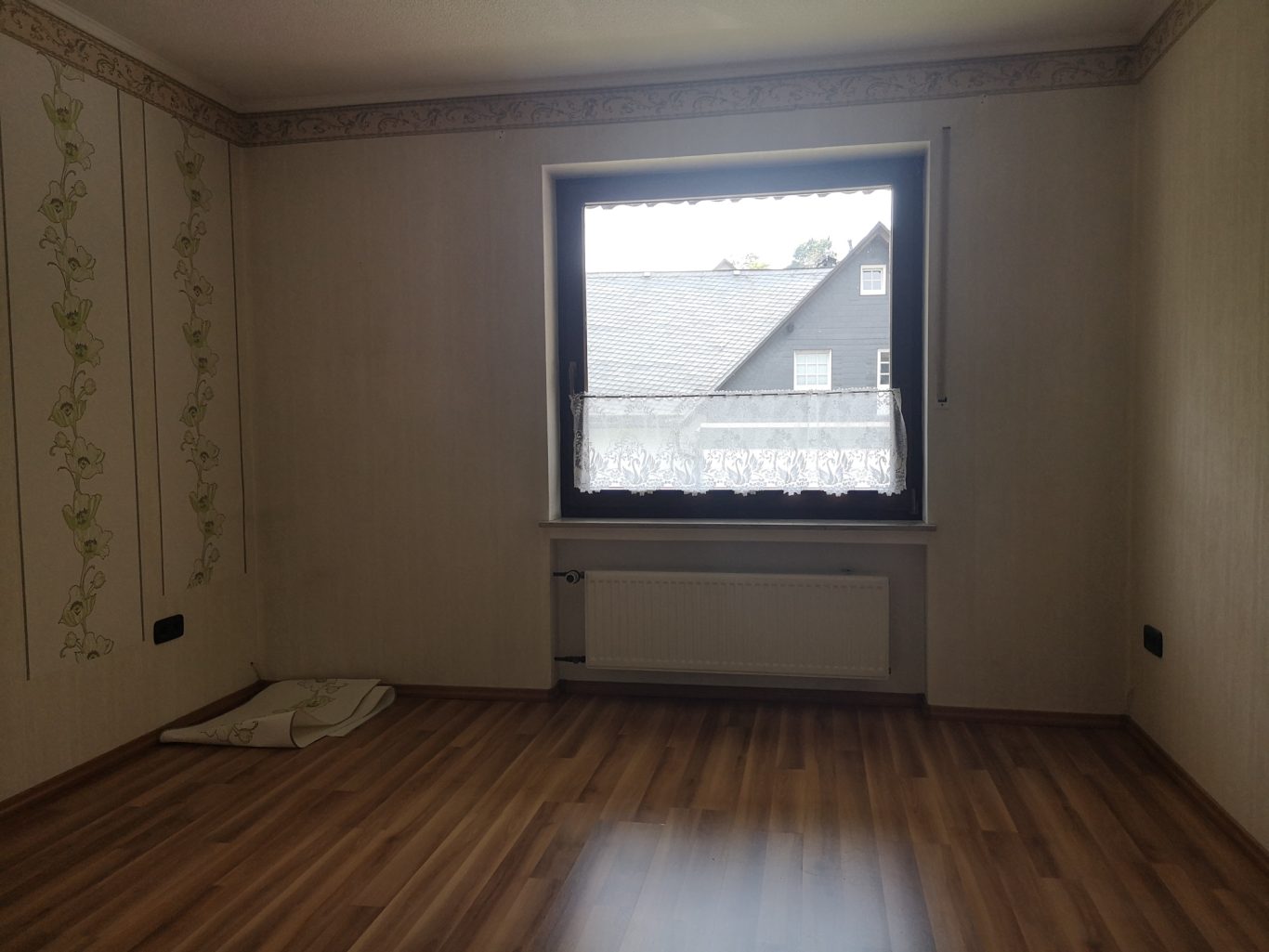 Immobilienmakler Münster Leere Wohnung mit Fenster, Holzboden und zwei Wänden mit leichtem Dekor.