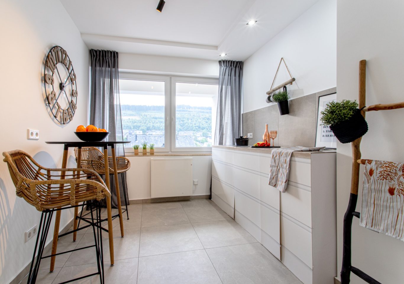 Immobilienmakler Münster Moderne Küche mit weißen Möbeln, Fenster und Barhockern. Früchte und Dekoration sichtbar.