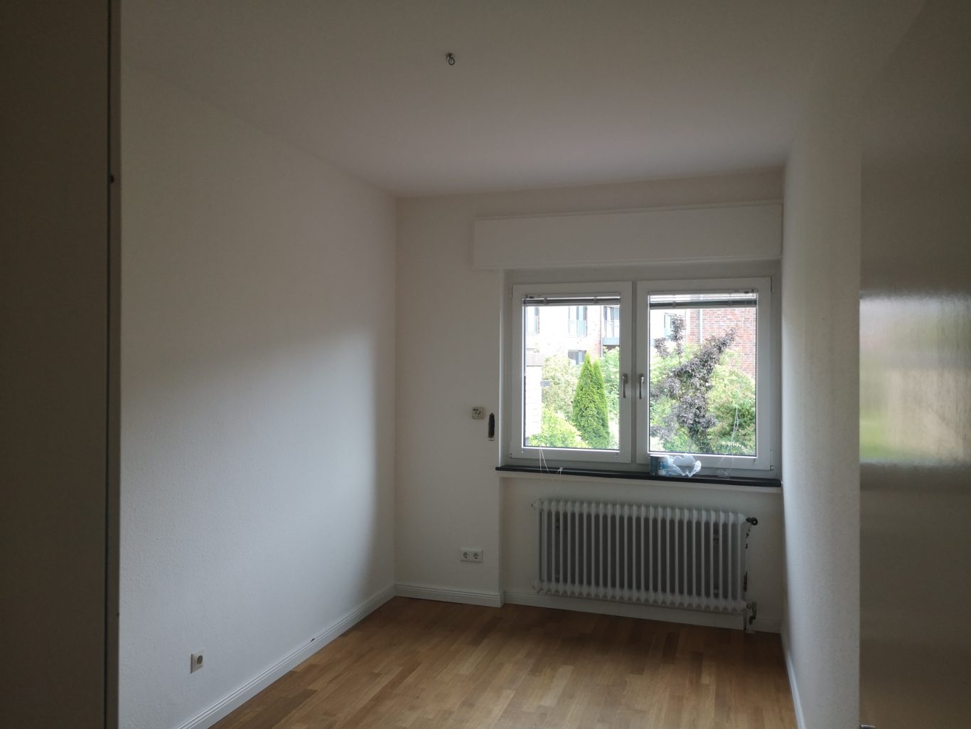 Wohnung mieten Leerer Raum mit weißen Wänden, Fenster zur Gartenseite und Holzfußboden.