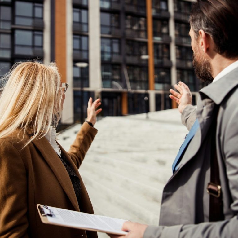Zinsentwicklung Haus Zinsentwicklung bei Hausverkauf: Zwei Personen zeigen auf ein modernes Gebäude mit großen Fenstern und Treppen.