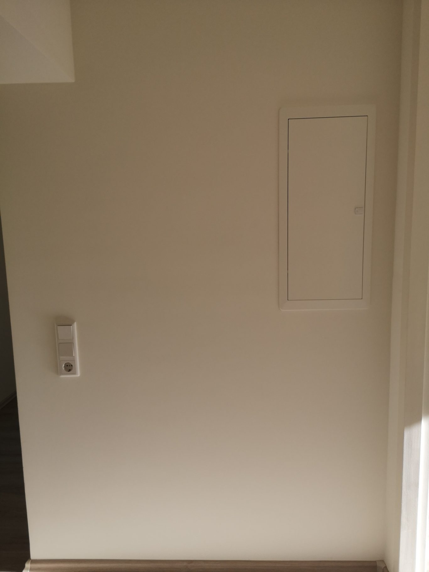 Immobilienmakler Münster Weiße Wand mit einem kleinen Zugangsklappen und einem Lichtschalter.