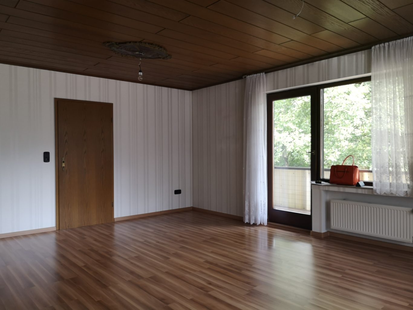 Immobilienmakler Münster Heller Raum mit Holzfußboden, großen Fenstern und einer Tür. Minimalistische Einrichtung.