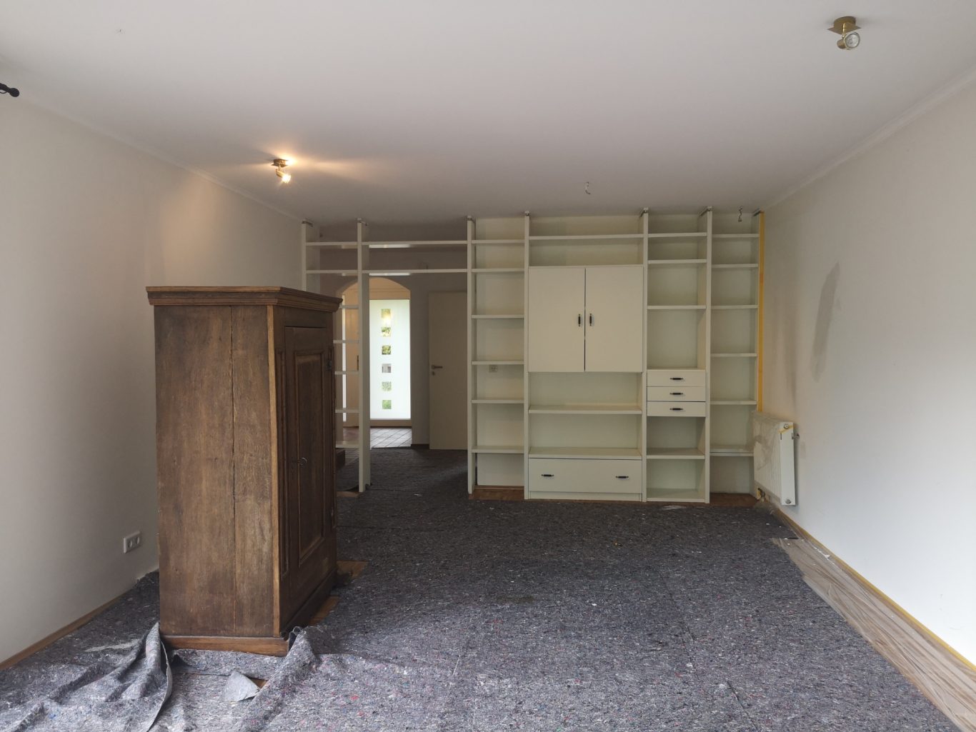 Wohnung kaufen Leerer Raum mit Teppich, Holzmöbel und einer großen, hellen Schrankwand.