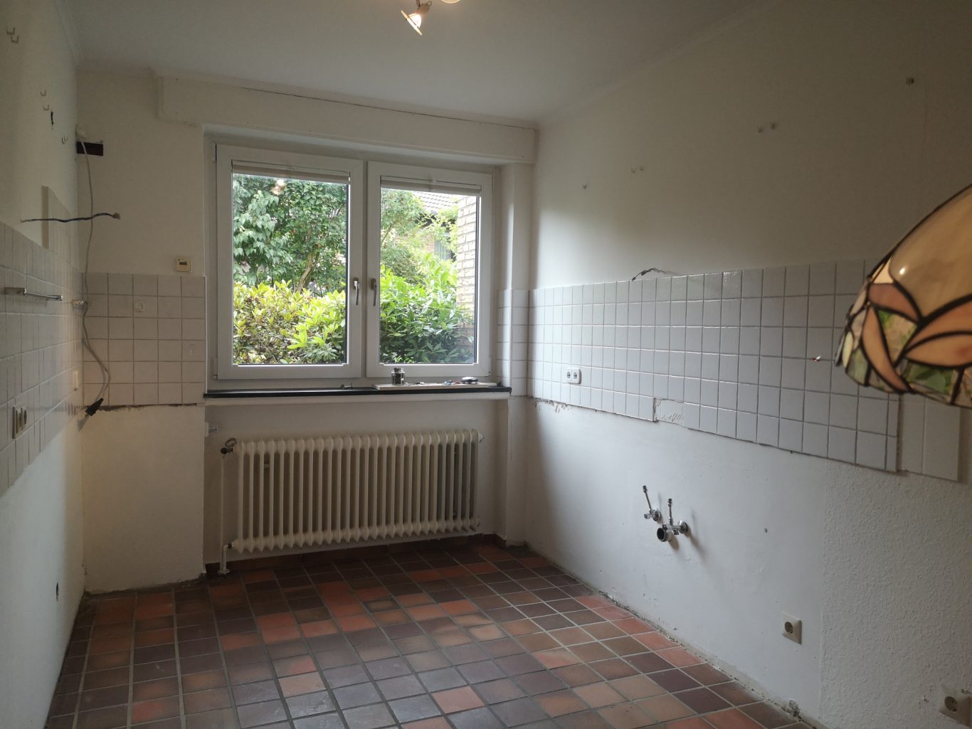 Wohnung verkauf Leere Küche mit zwei Fenstern, Sicht ins Grüne und buntem Lampenschirm.