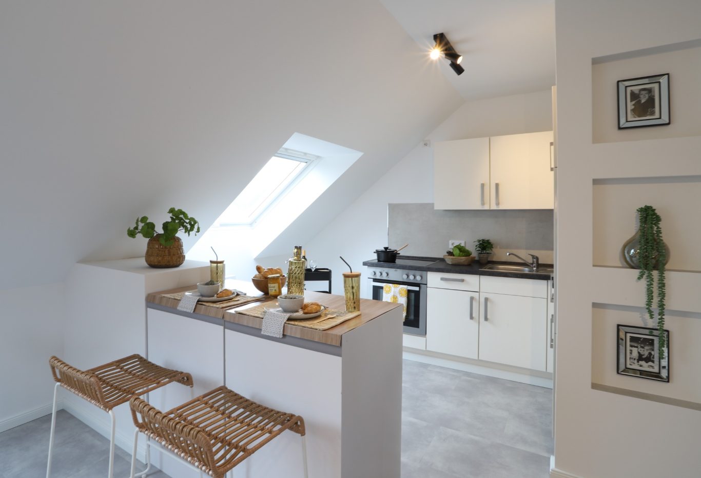 Immobilienmakler Münster Moderne Küche mit abgewinkeltem Dach, hellen Möbeln und Barstühlen aus Holz.