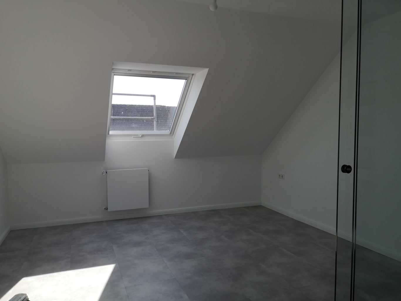 Immobilienmakler Münster Heller, leerer Raum im Dachgeschoss mit schrägen Wänden und Fensterausschnitt.